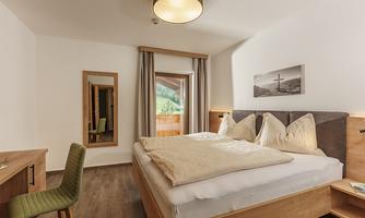 A cozy bedroom with a large bed and elegant wood paneling. The room has a window overlooking nature and a stylish decor.