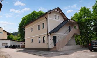 A modern two-story building on a quiet street.  
Surrounded by trees and other buildings.
