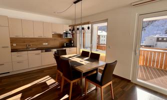 A bright, modern kitchen with a dining table and chairs. Plenty of daylight streams through the windows, illuminating the space.