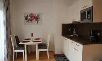 A modern kitchen with a small table and chairs. A floral picture hangs on the wall, and the decor is bright and inviting.