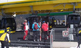 A cable car station in the mountains with skiers just getting on. In the background, snow-covered landscapes can be seen.