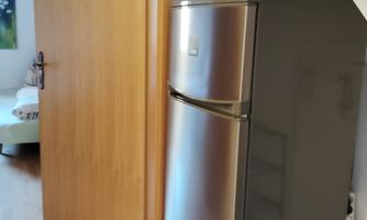 A modern kitchen with a silver refrigerator and a microwave on top. In the background, there is a door leading to another room.