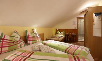 A cozy bedroom in the attic with two beds and colorful bedding. The room features a shower and a warm, inviting atmosphere.