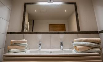A modern bathroom with a double sink and a large mirror. Neatly folded towels are placed beside the sink.