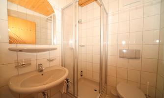 A small bathroom with a shower cabin, a sink, and a toilet. The walls are tiled and the floor is light.