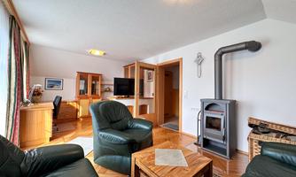 A cozy living space with two green armchairs and a wooden table. In the background, there is a television and a stove.