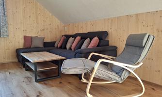 A cozy seating area with a dark couch, cushions, and a wooden coffee table. Next to the couch is a comfortable, adjustable armchair.