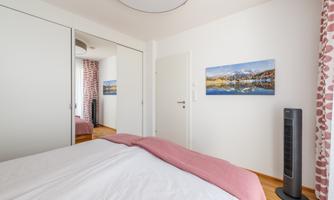 A modern bedroom with a colorful picture on the wall. The room is bright and has large mirrored wardrobes as well as a fan.
