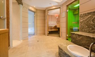 A modern wellness area with stone floors and colored light accents. The environment features a sauna and shower areas for relaxation.