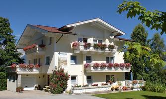 A beautiful, multi-story house with balconies and blooming flowers. It stands in a green setting under a clear sky.