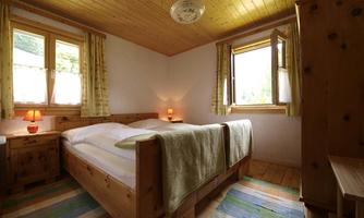 A cozy bedroom with a double bed and wooden decor. Large windows let in plenty of daylight.