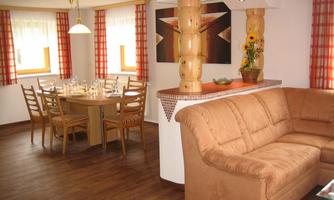 A cozy living space with a large dining table and chairs. In the foreground is a comfortable, brown sofa.