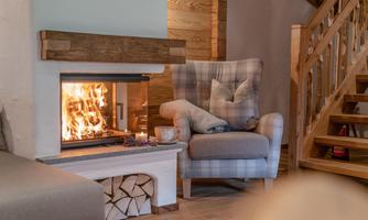 A cozy room with an armchair and an open fireplace. The fire is burning and creates a warm atmosphere.