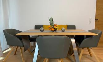 A modern dining table made of wood with gray chairs. On the table is a fresh fruit bowl and a decorative plant.