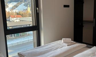 A modern bedroom with a large window that offers a view of the mountains. The beds are neatly made with white bedding.