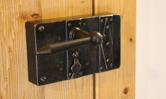 A timeless black metal door lock on a wooden paneling. It features a classic design with a lever and decorative elements.