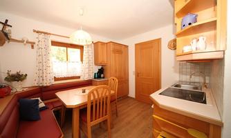 A cozy kitchen with wooden cabinets and a dining area. On one wall, there is a windowsill with curtains.