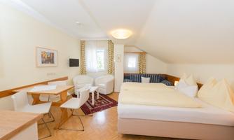 A bright attic room with a double bed, a small table, and two chairs. Pictures are hanging on the wall, and the light is pleasantly soft.