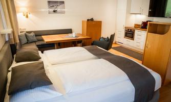 A modern room with a double bed and a cozy seating area. The small kitchenette is well-equipped and invites relaxation.