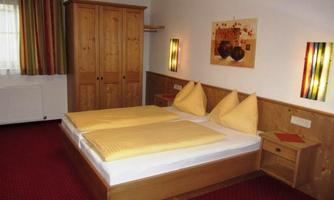 A cozy bedroom with a double bed and yellow pillows. The walls are painted in warm tones and decorated with modern pictures.
