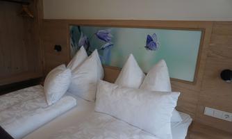A cozy bedroom with a double bed, large pillows, and a decorative wall with floral motifs. The wooden paneling creates a warm and inviting atmosphere.