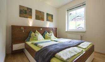 A bright bedroom with a double bed and colorful pillows. On the walls are modern artworks and a window overlooking the surroundings.