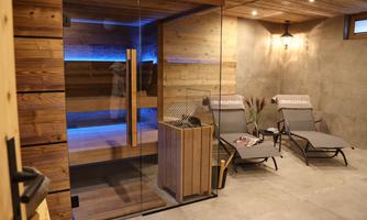 A modern wellness area with a sauna and cozy loungers. The walls are wooden, and gentle blue lighting creates a relaxed atmosphere.