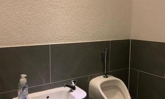 A simple bathroom with a sink and a urinal. The walls are tiled in neutral tones.