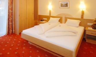 A cozy hotel room with a large bed and wooden furniture. The warm colors and carpet design create an inviting atmosphere.