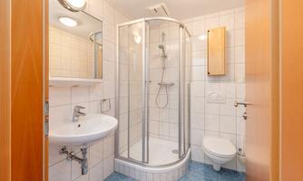 A modern bathroom with a shower, sink, and toilet. The walls are tiled and the floor has an attractive pattern.