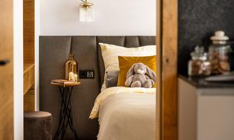 A cozy bedroom with a bed decorated with yellow pillows. On the nightstand, there is a vase and a stuffed animal.
