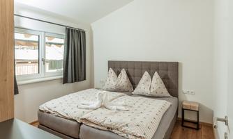 A modern bedroom with a double bed and minimalist furniture. Large windows let in plenty of light and the walls are designed in a light color.