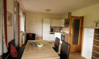 A modern kitchen with a wooden dining table and black chairs. It is bright and friendly, furnished with white cabinets and a window that lets light in.