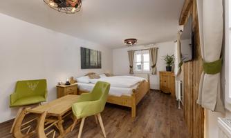 A cozy room with a large double bed and two green chairs. Wood paneling and decorations create a pleasant atmosphere.