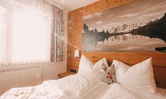 A cozy room with wooden walls and large cushions. In the background, there is a beautiful landscape picture of mountains and a lake.