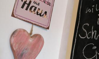 A handcrafted wooden heart hangs on the wall. Above it is a sign that reads "Daily laughter brings sunshine into the home."