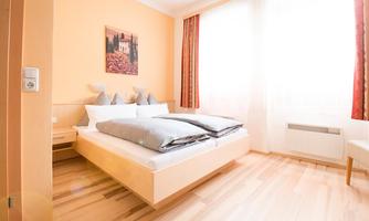 A bright and modern bedroom with a large bed and wooden floor. The windows let in plenty of daylight and the walls are painted in warm colors.