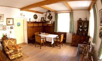 A cozy room with wood decor and a table in the middle. Pictures hang on the walls, and there are various pieces of furniture.