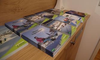 A collection of brochures is neatly arranged on a table. The brochures showcase outdoor activities in a wintry landscape.