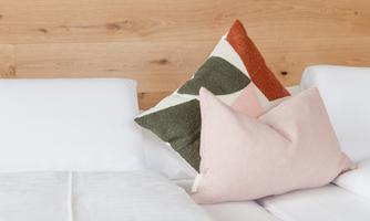 A cozy bed with white bedding and decorative pillows in soft colors. The wall behind the bed is painted in a soothing green shade.