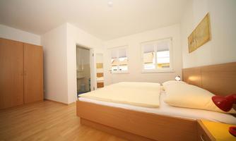 A bright bedroom with a double bed and a wooden wardrobe. The walls are painted in neutral colors, and the room feels friendly and inviting.