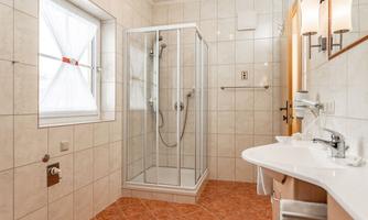 A modern bathroom with a glass shower and a sink. The walls are light tiled and the floor has a warm color scheme.