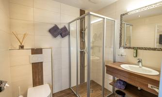 A modern bathroom with a shower cabin, a sink, and an elegant wooden shelf. Bright tiles and stylish details create an inviting atmosphere.