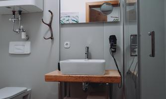 A modern bathroom with a white sink on a wooden table. In the background, there is a shower and wall paneling in neutral colors.