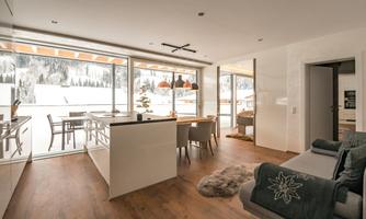 A modern apartment with large windows and a view of the snow-capped mountains. The space is bright and cozy with a stylish table and comfortable furniture.