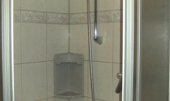 A modern shower cubicle with white tiles and a chrome showerhead. The surroundings are designed to be simple and functional.