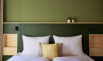 A stylish bedroom with two beds and a green wall. Decorative pillows and plants create a cozy atmosphere.