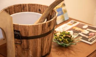 A wooden bucket with a long handle stands on a table. Next to it are some magazines and a bowl with green leaves.