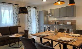 Modern kitchen furniture with a dining table and a cozy living room. Bright windows create a friendly atmosphere.
