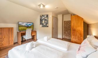 A modern bedroom with two beds and a desk. The room has a warm atmosphere and a TV corner.